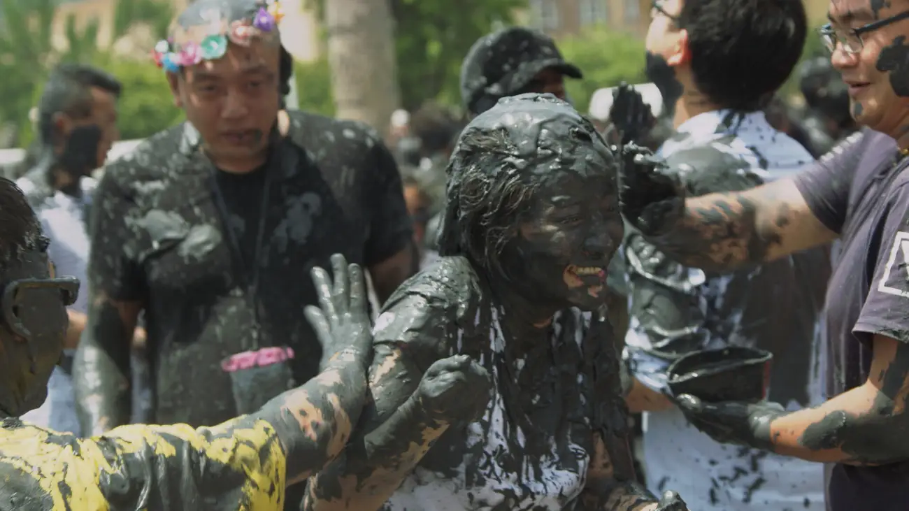 A laughing young girl getting covered in black mud by Chinese festivalgoers.