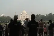 Sillhouetted tourists with the sunlit Taj Mahal in the background.