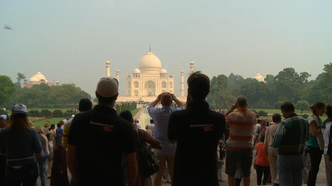 Sillhouetted tourists with the sunlit Taj Mahal in the background.