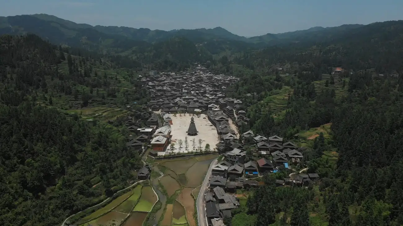 An aerial view of a traditional Dong village and drum tower amongst the lush mountains.