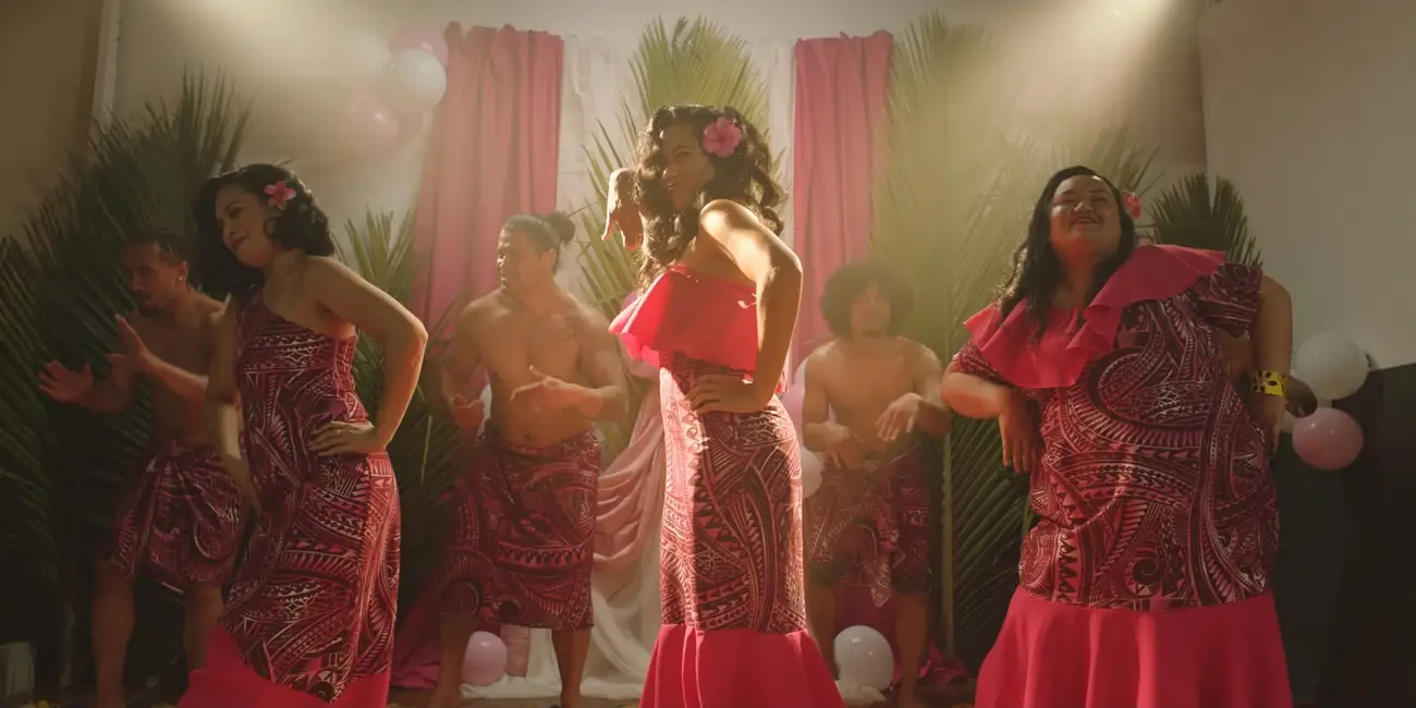 Three Samoan women dance on stage in bright, modern Pacific Island dresses.